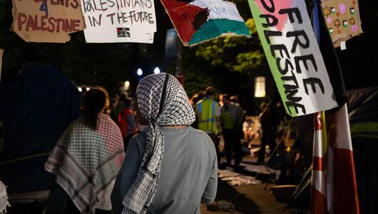 Eine Frau im Kopftuch läuft unter einem "Free Palistine" Schild durch