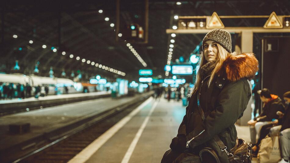 Frau steht an Bahnsteig und wartet auf Zug