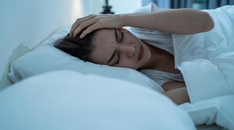 Frau liegt im Bett und hält sich den Kopf