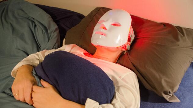 Frau zu Hause mit LED-Maske im Bett