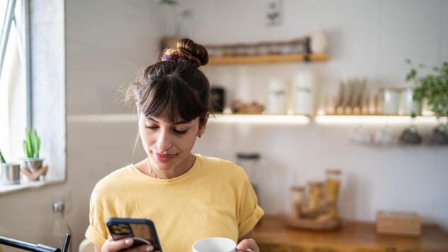 Frau steht in der Küche und blickt aufs Handy 