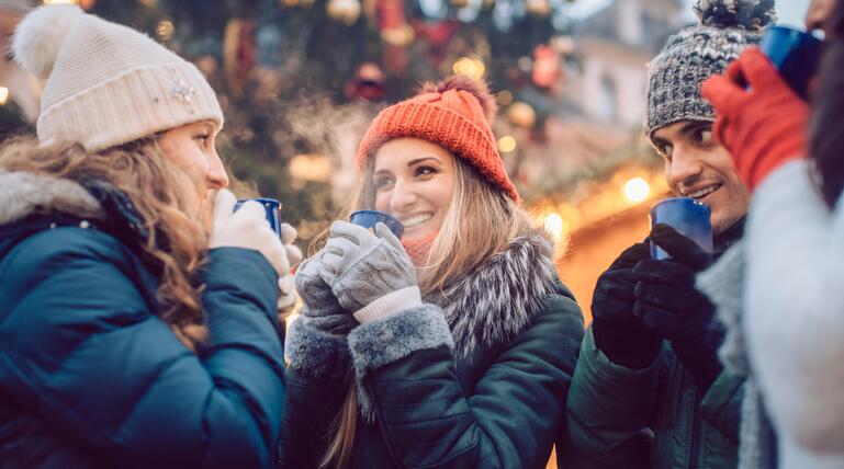 Lachende Weihnachtsmarktbesucher trinken Glückwein.