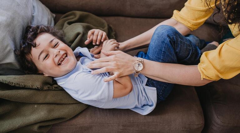Mutter kitzelt Kind auf der Couch