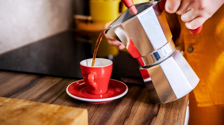 Frau gießt Kaffee in eine rote Tasse