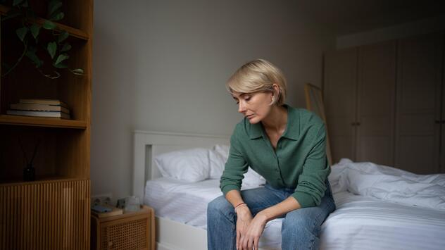 Eine Frau sitzt auf ihrem Bett und schaut bekümmert auf den Boden.